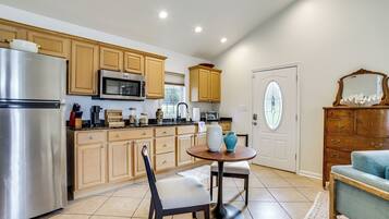 A kitchen with wooden cabinets, a stainless steel refrigerator, a microwave, and a dining area with a table and chair.