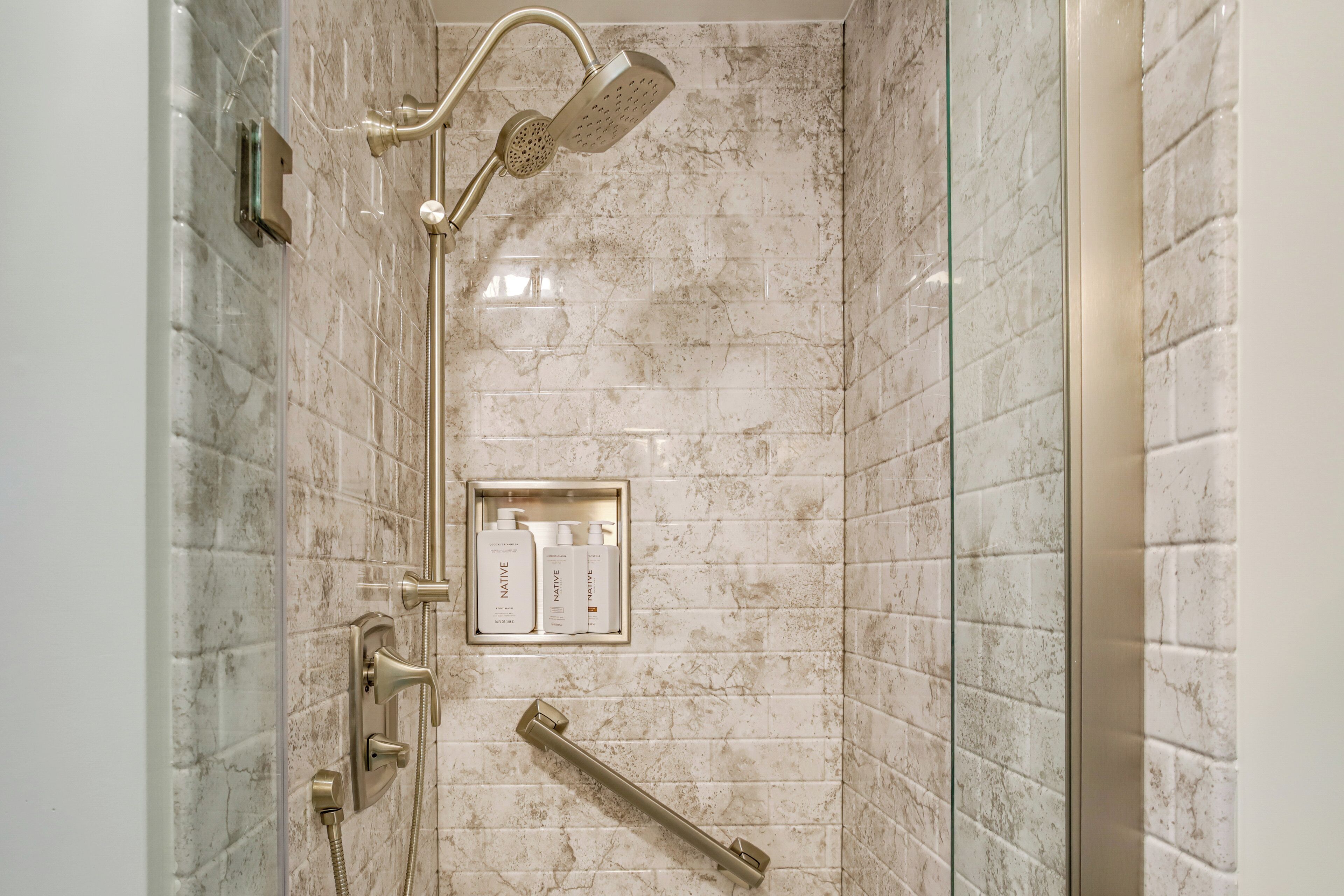 A shower with a handheld showerhead, a wall-mounted control panel, and a glass-enclosed shower area.