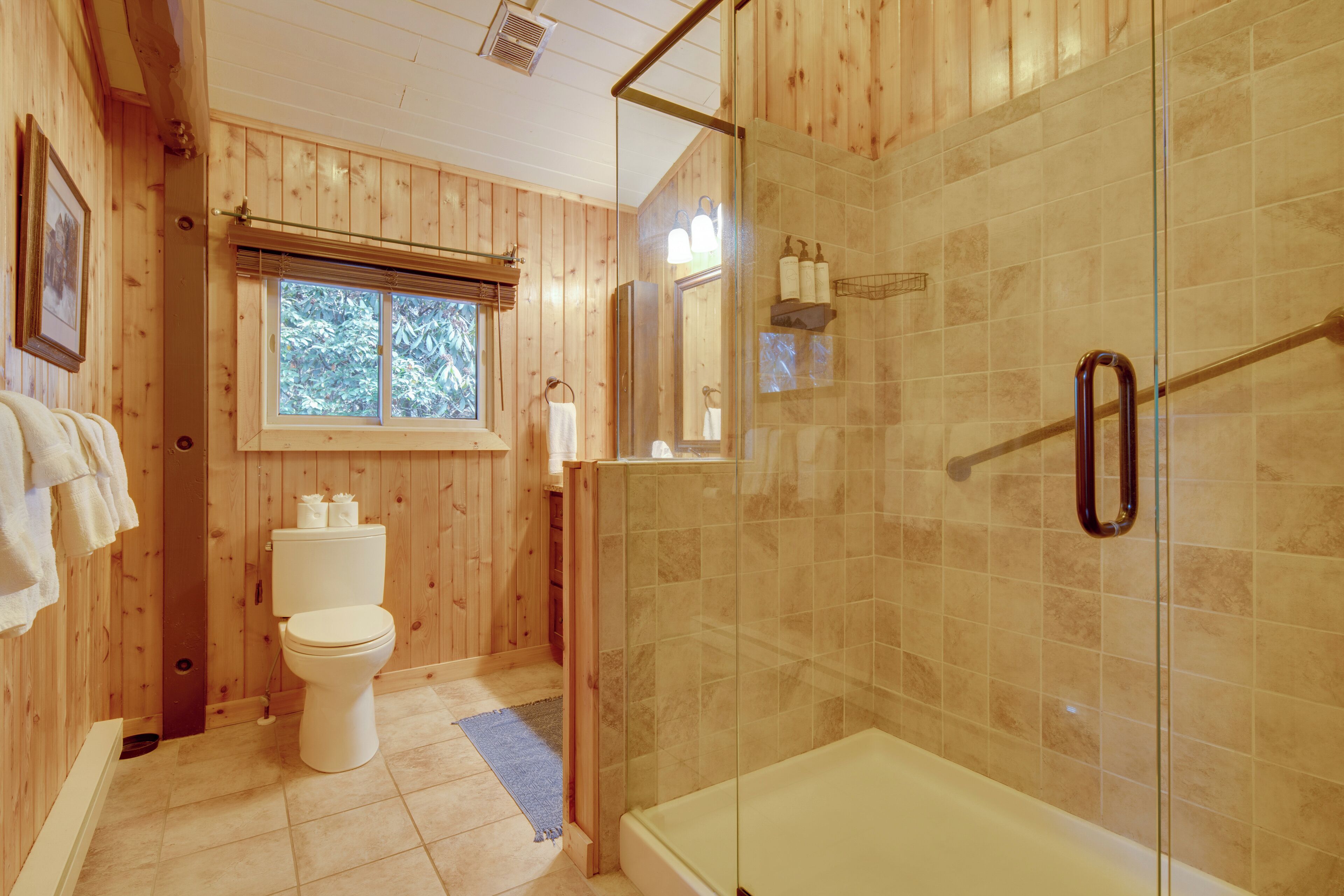 A wooden-paneled bathroom with a toilet, a glass-enclosed shower, and a bathtub.