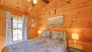 A wooden cabin bedroom with a bed, two bedside lamps, a window with curtains, and a painting on the wall. - Steps to Virginia Creeper Trail: Creekside Retreat (Damascus)