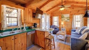 A cozy cabin with wooden interiors, a kitchen with a sink and stove, a dining area with a table and chairs, and a living room with a sofa and a television. - Steps to Virginia Creeper Trail: Creekside Retreat (Damascus)