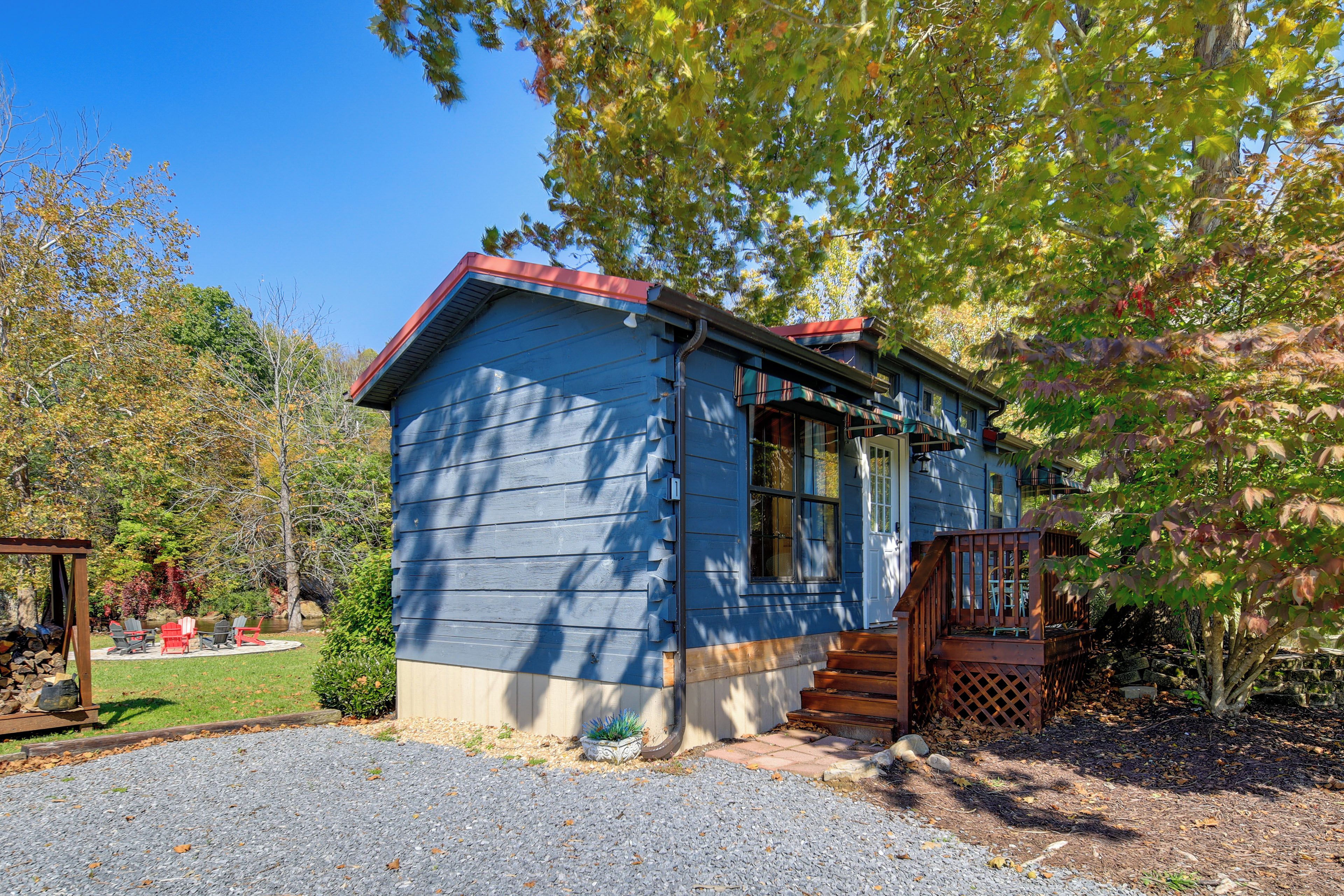 A small blue house with a red roof, a porch, and a gravel driveway.