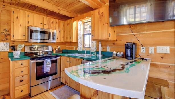 A wooden cabin kitchen with a large island, stainless steel appliances, and a window with curtains. - Steps to Virginia Creeper Trail: Creekside Retreat (Damascus)