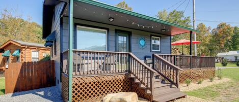 A cabin with a deck, a covered porch, and a large rock in front.
