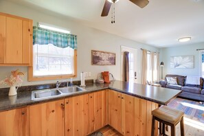 A kitchen with wooden cabinets, a sink, and a window with a checkered curtain. - Trail Town Usa! 2BD Cabin on Laurel Creek w/ Deck (Damascus)