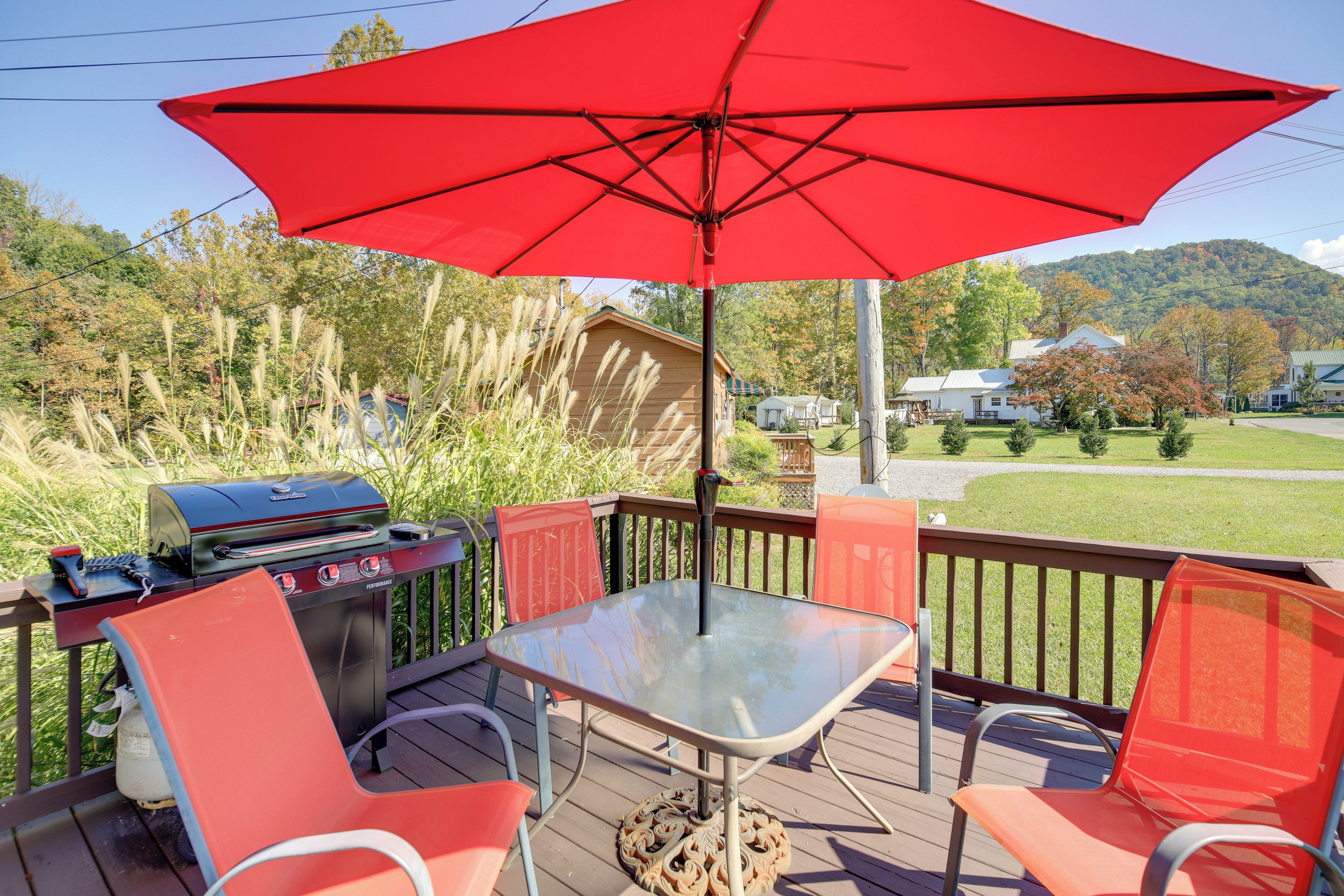 A deck with a barbecue grill, a glass table, and red chairs.