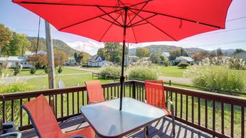 A deck with a table and chairs, an umbrella, and a view of houses and hills in the background.