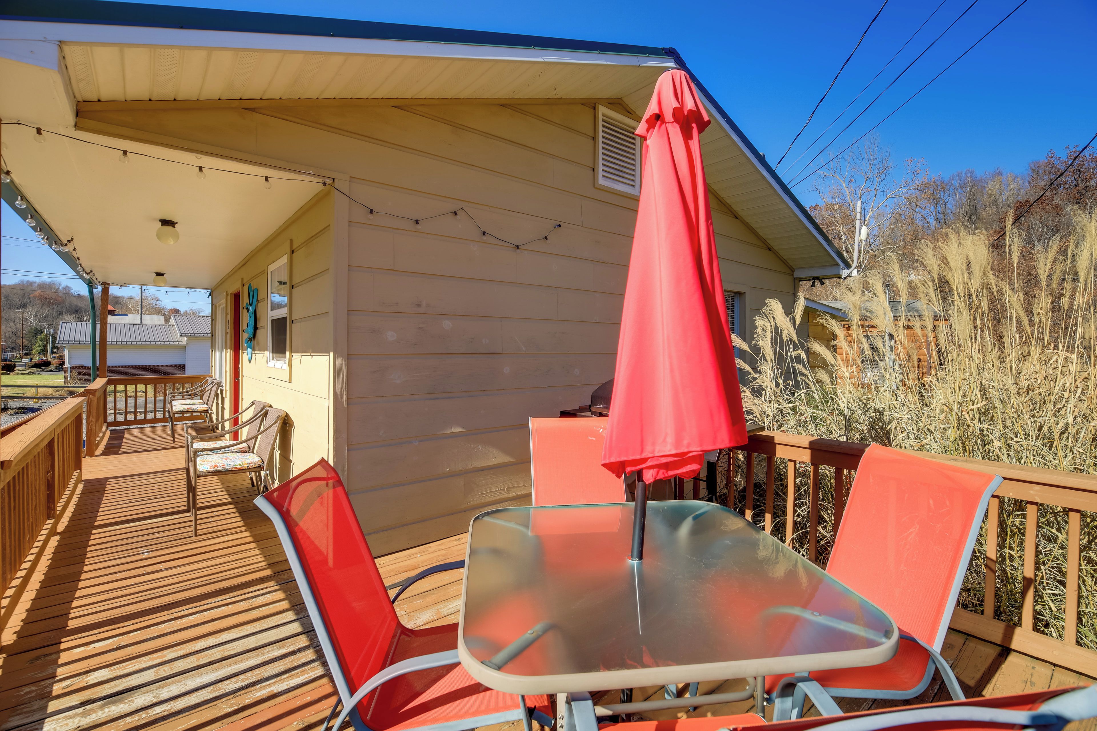 A covered outdoor deck with a table and chairs, a red umbrella, and a view of the surrounding area.