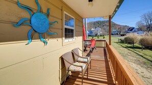 A covered porch with a sun decoration, two wicker chairs, and a view of a green landscape.