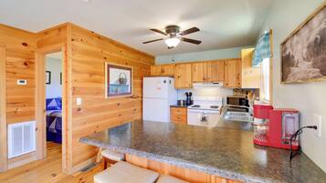 A compact kitchen with wooden cabinets, a granite countertop, a ceiling fan, and a red coffee maker.