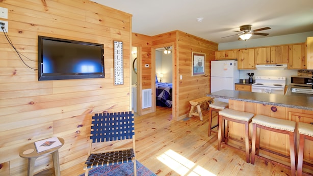 A wooden cabin interior with a TV, wooden bar stools, a small table, and a ceiling fan.