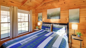 A wooden cabin bedroom with a large bed, two bedside tables with lamps, and a window with curtains. - Pet-friendly Damascus Cabin w/ Deck & Mtn Views! (Damascus)