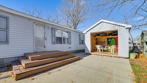 A mobile home with a garage door open, revealing a dining area with chairs and a table. - Walk to Houghton Lake! Family Retreat w/ Patio (Houghton Lake Heights)
