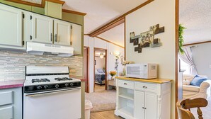 A kitchen with a stove, microwave, and cabinets. There is a chair and a plant in the room. - Walk to Houghton Lake! Family Retreat w/ Patio (Houghton Lake Heights)