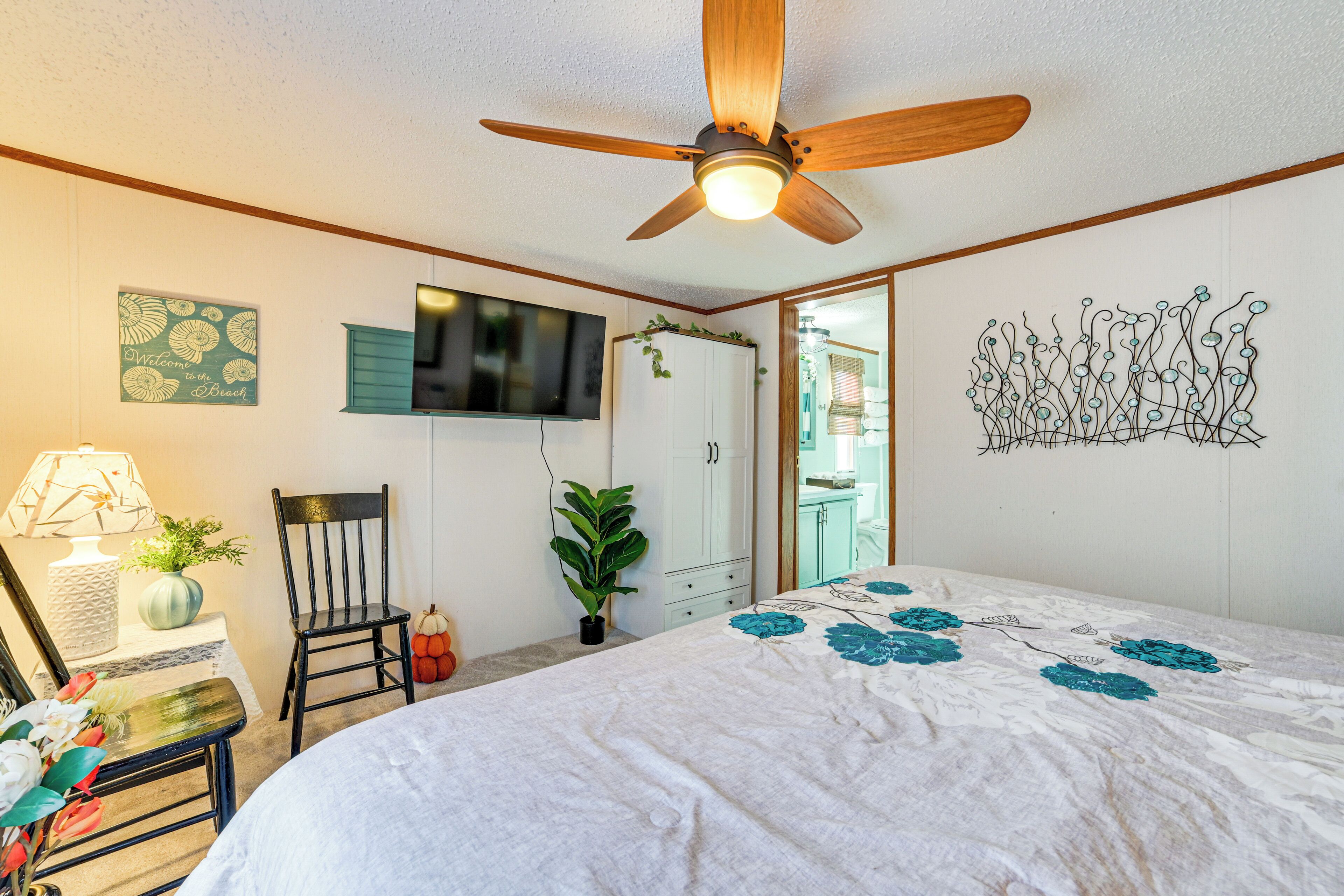 A bedroom with a bed, a ceiling fan, a TV, a plant, and a wall art piece.