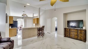 A spacious living area with a marble floor, a large wooden cabinet, a television, and a ceiling fan. - Spacious Home w/ Yard: 8 Mi to Wabasso Beach (Sebastian)