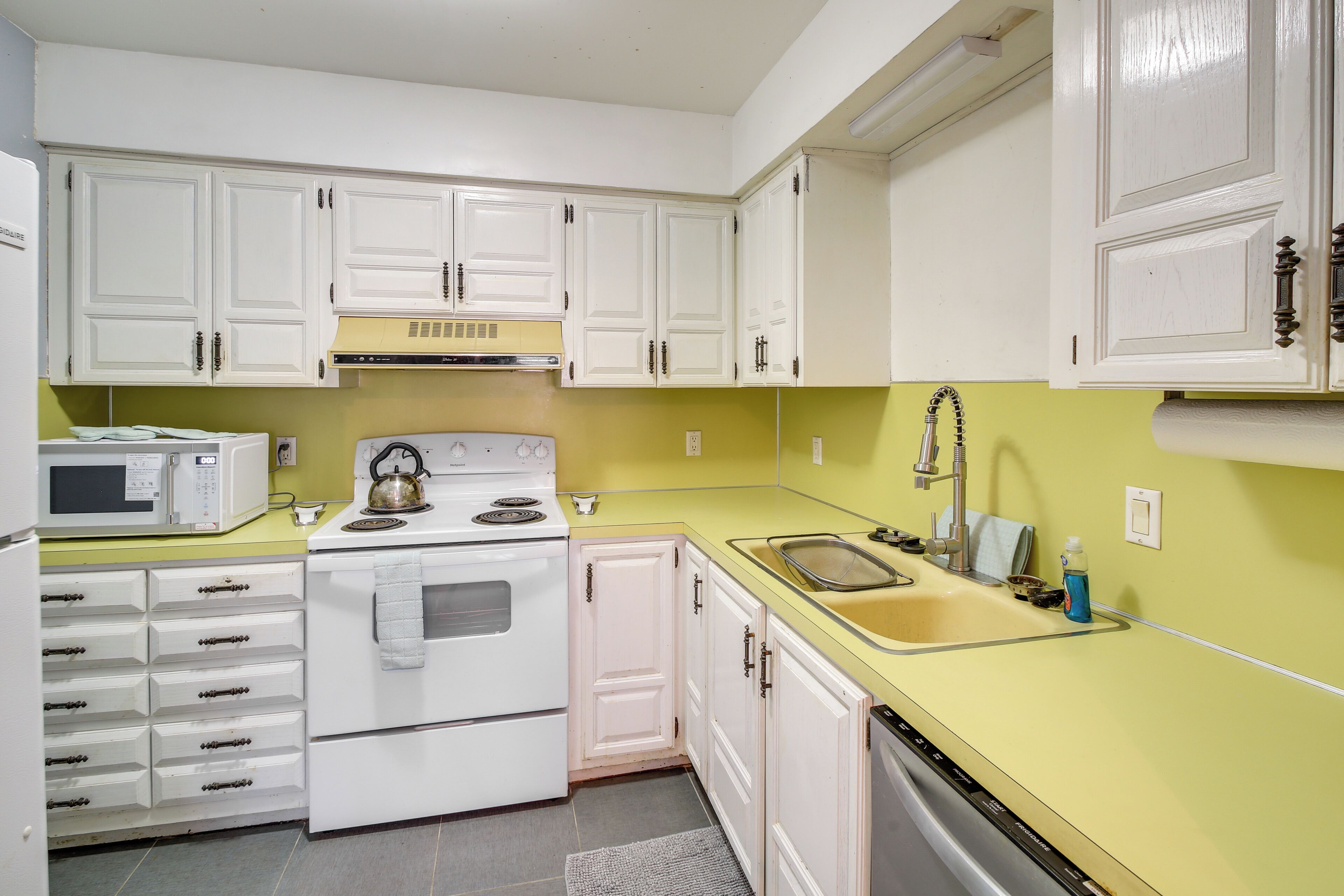 A kitchen with white cabinets, a microwave, an oven, a sink, and a dishwasher.