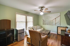Una sala de estar con ventilador de techo, un sofá blanco, una mesa de centro de madera y un mueble de madera.
