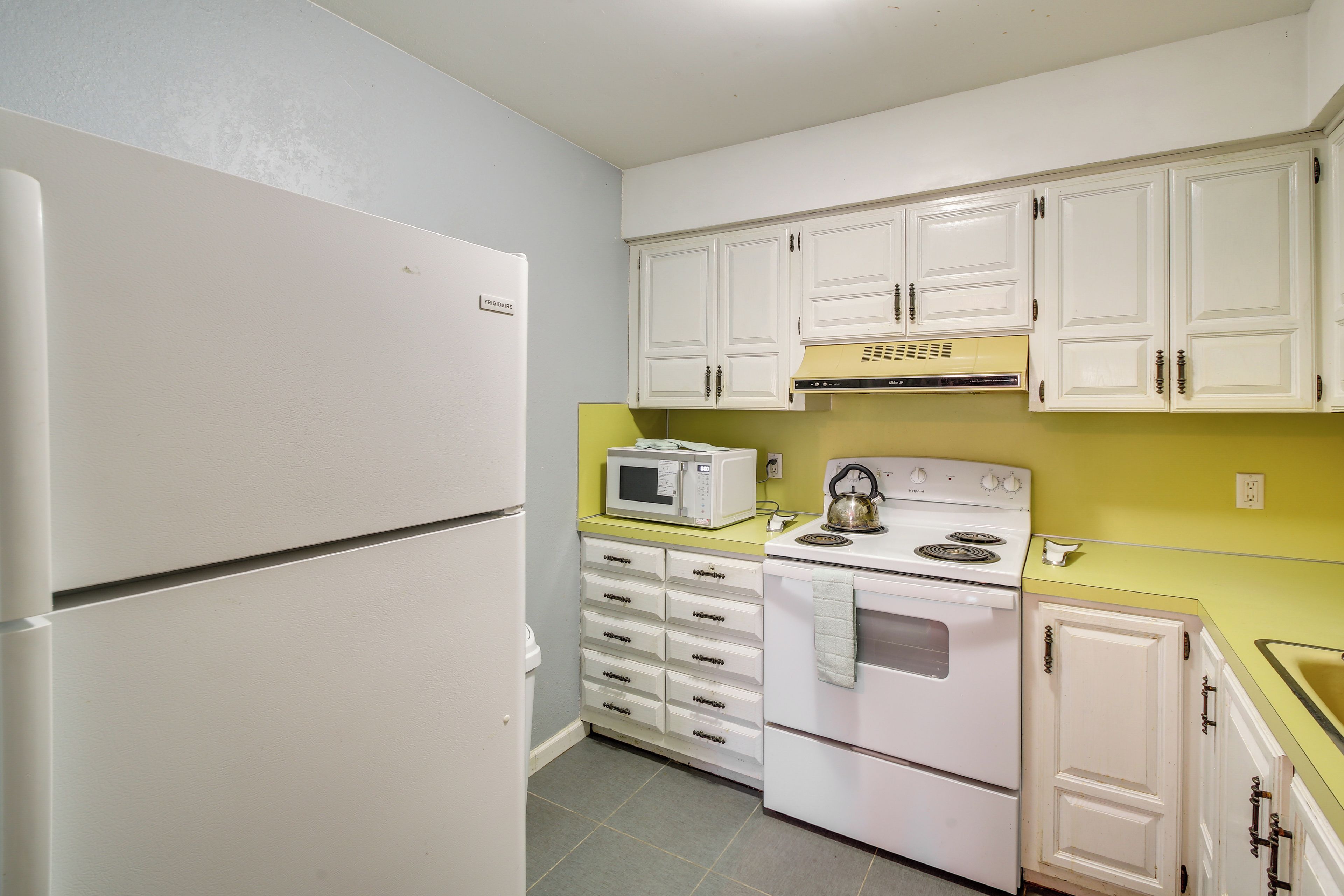 A compact kitchen with white cabinets, a microwave, a stove, and a refrigerator.