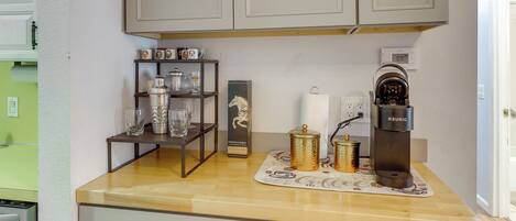 A kitchen with a coffee maker, a shelf with glassware, and a decorative item on the counter.