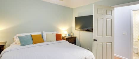 A bedroom with a bed, a nightstand, a ceiling fan, and a door leading to another room.