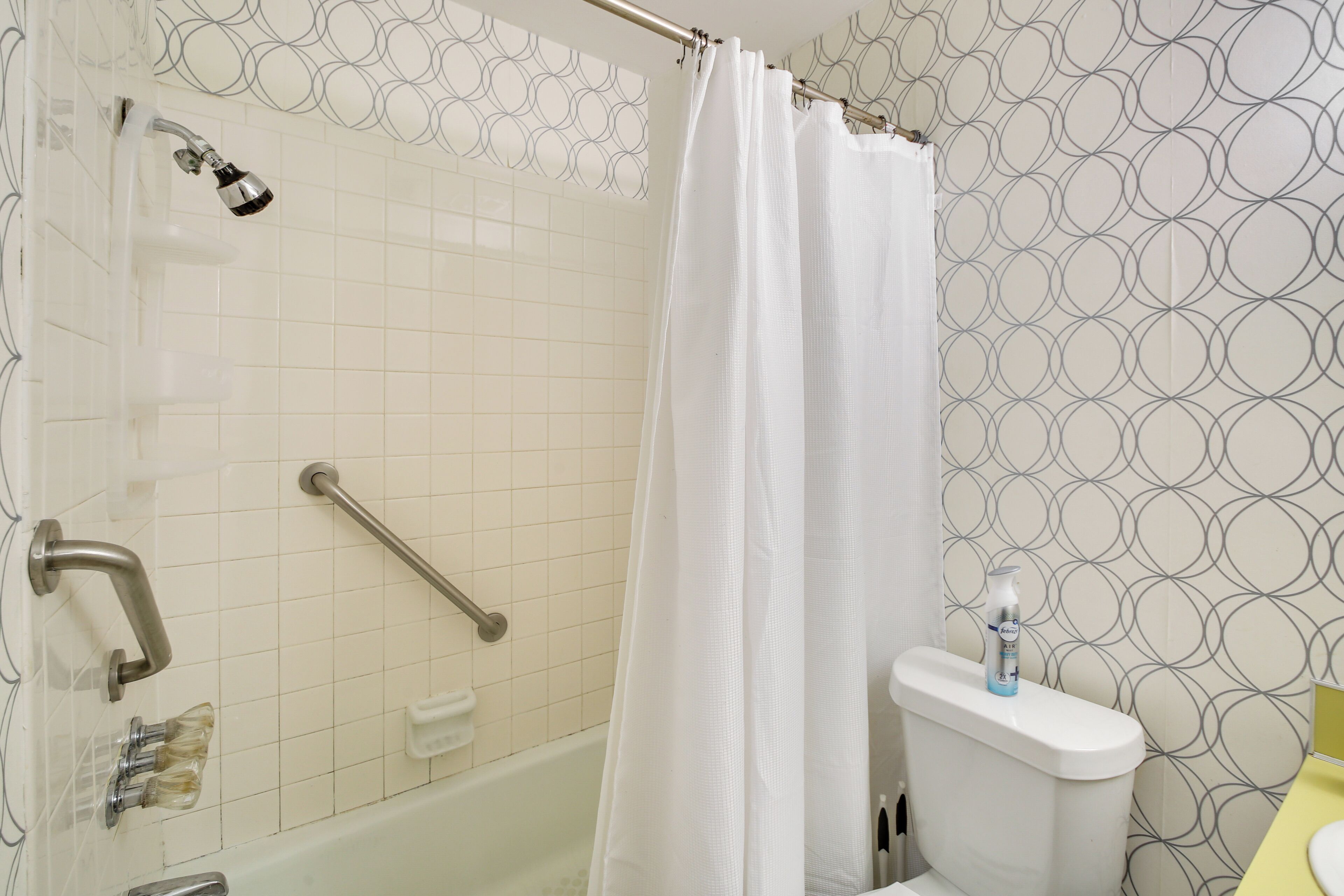 A bathroom with a shower, toilet, and a handrail.