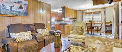 A living room with a brown leather sofa, a wooden coffee table, and a painting of horses on the wall.