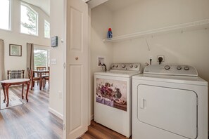 Een wasserette met een wasmachine, droger en een wandplank met een fles.