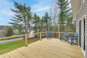 Eine Holzterrasse mit Geländer, drei blaue Stühle und Blick auf Bäume und eine Straße.