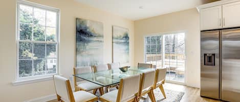 Een eethoek met een glazen tafel, stoelen, grote ramen en een roestvrijstalen koelkast.