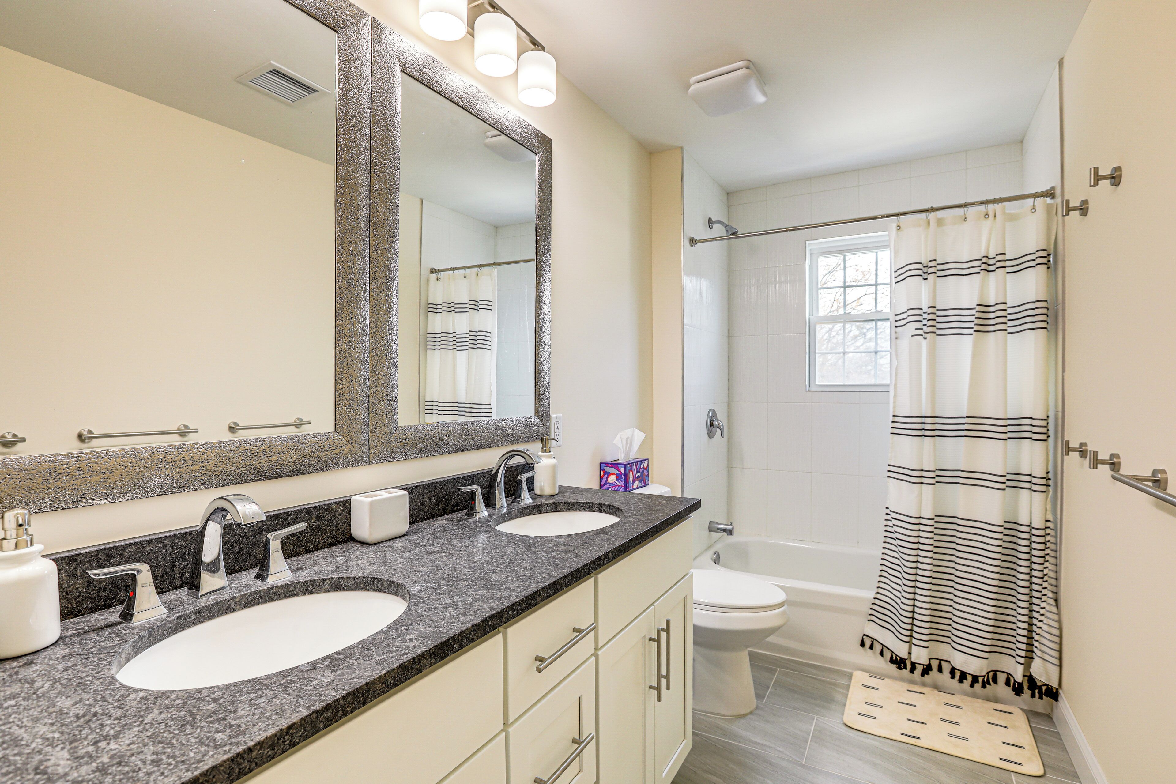 A bathroom with two sinks, a large mirror, a shower with a striped curtain, and a small window.