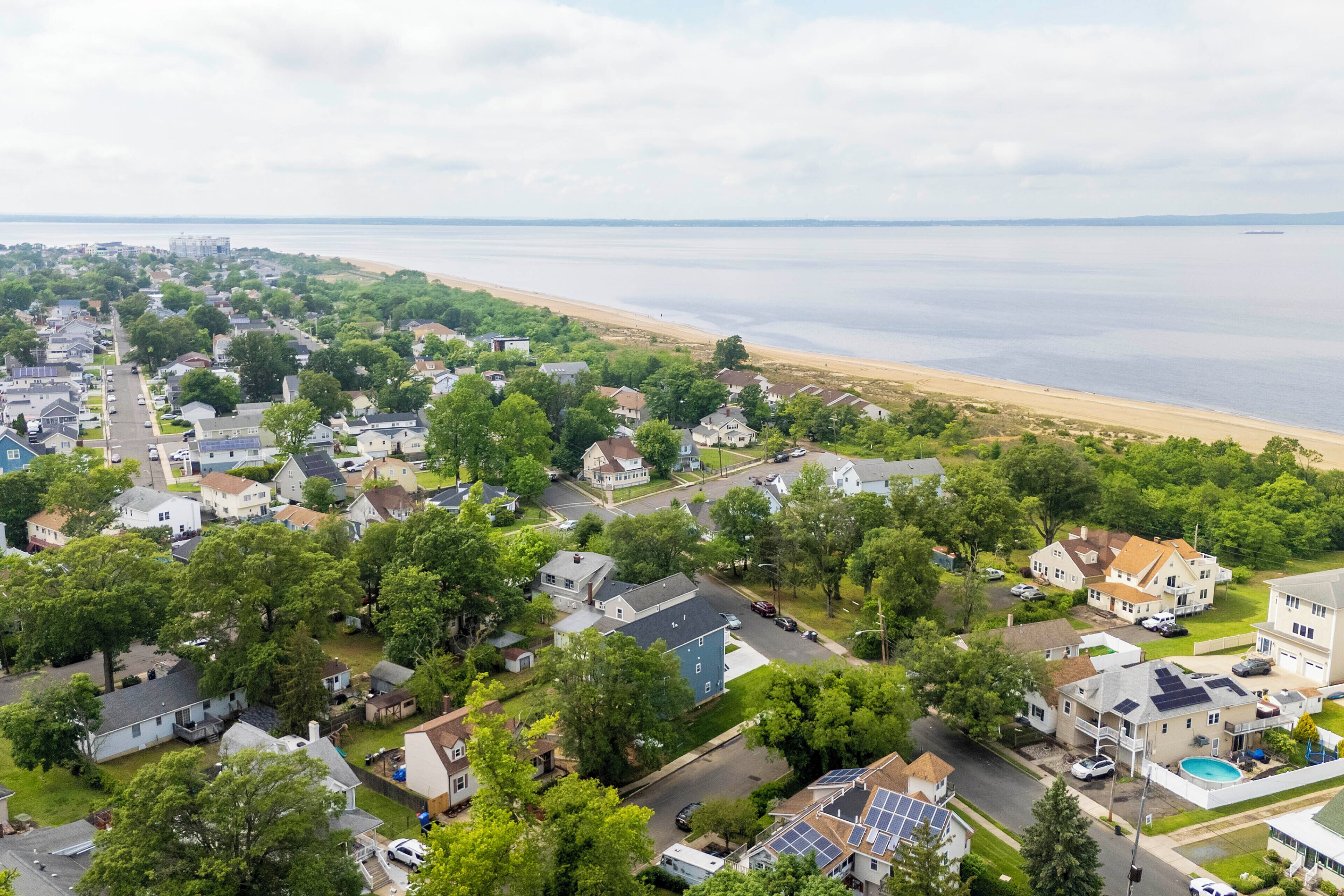 An aerial view of a residential area with houses, trees, and a beach.