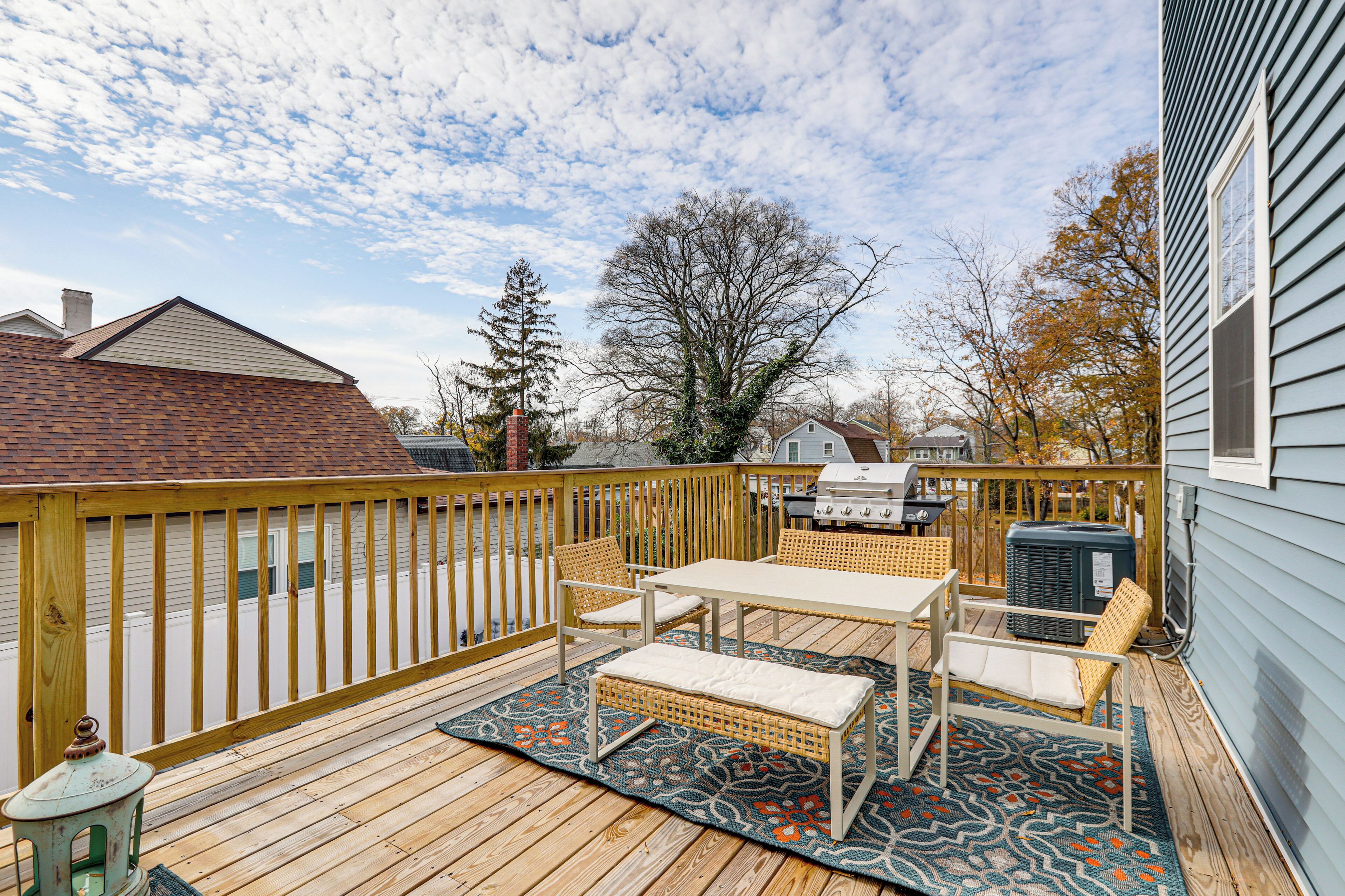 Une terrasse en bois avec une table et des chaises, un barbecue et un grand arbre en arrière-plan.