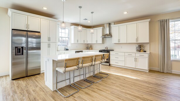 A modern kitchen with white cabinetry, a stainless steel refrigerator, a large island with bar stools, pendant lighting, and a window with curtains. - Walk to Keansburg Beach! Family Home w/ Pool (Keansburg)