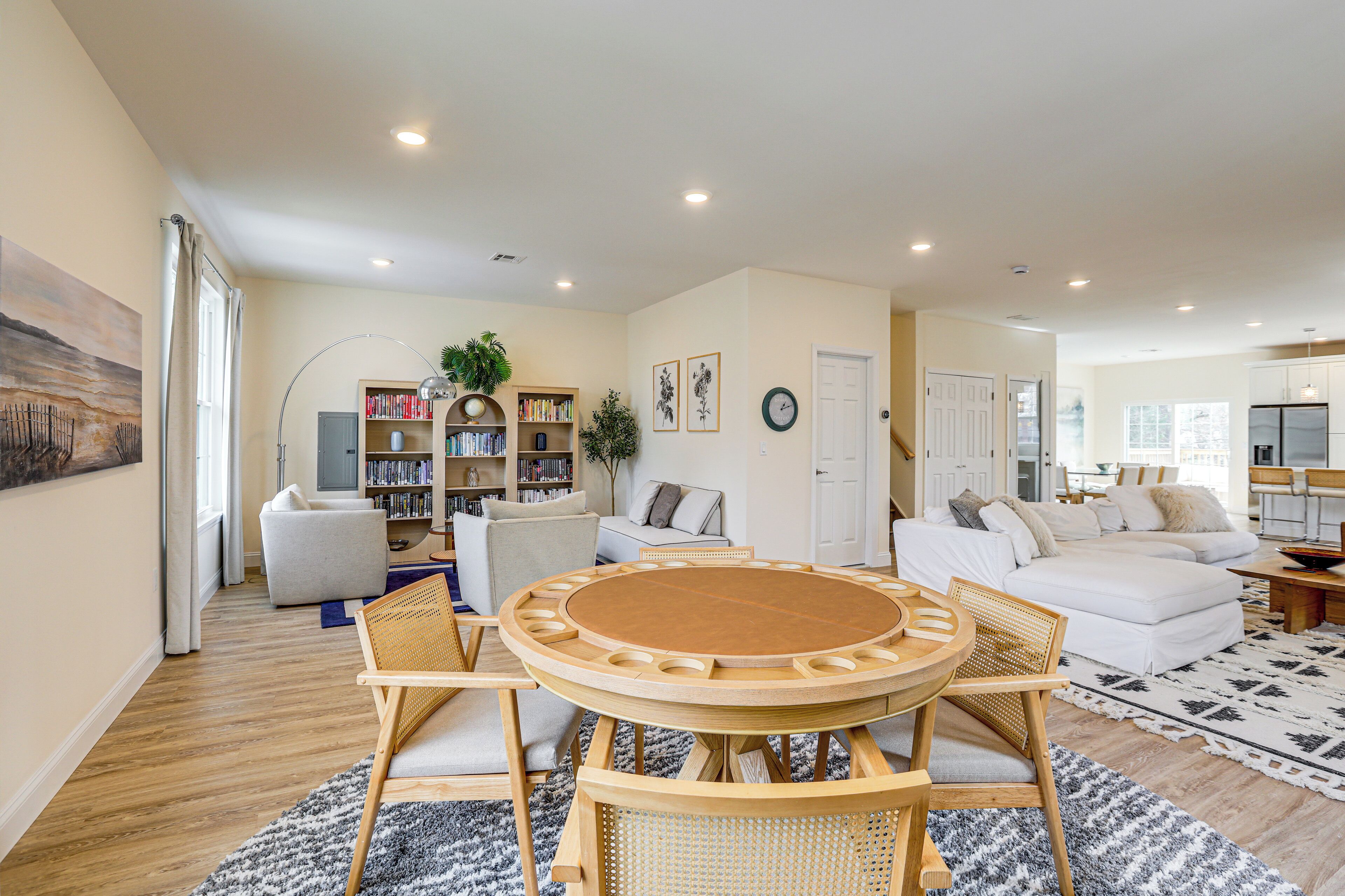 A spacious living room with a round wooden table and chairs, a sofa, a bookshelf, and a dining area.