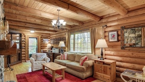 A log cabin interior with a wooden ceiling, a sofa, a coffee table, a lamp, and a stone fireplace. - Along Big Wood River: Hailey Family Cabin w/ Yard (Hailey)