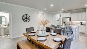 A modern kitchen with white cabinets, a central island, and a dining area with a wooden table and chairs. - Close to Energy Giants! 3,300-sq-ft Midland Home (Midland)