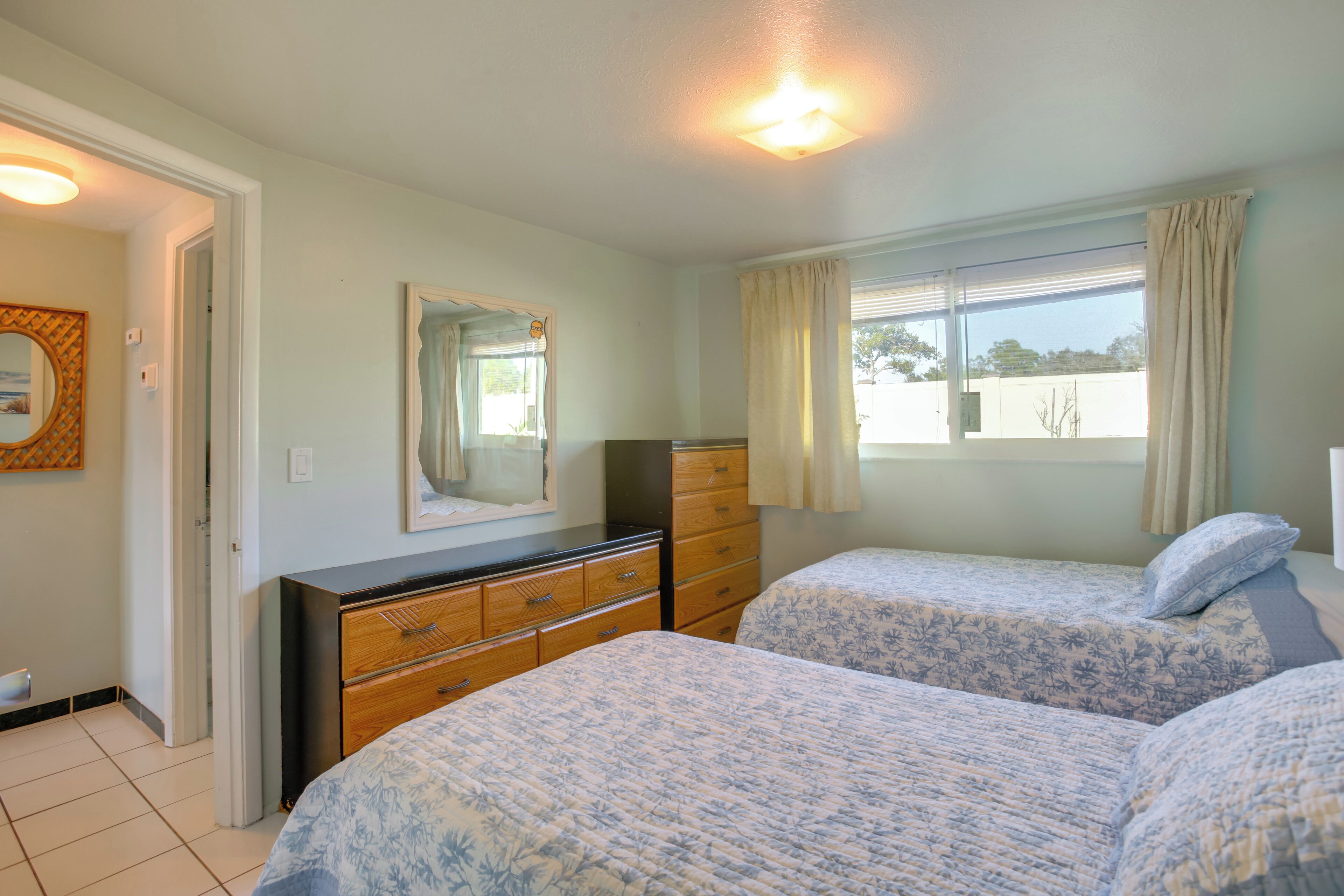 A bedroom with two beds, a dresser, a mirror, and a window with curtains.