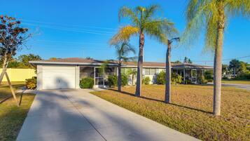 A single-story house with a garage, a front yard with palm trees, and a clear blue sky.