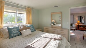 Une chambre à coucher avec un lit, une commode, un miroir et une fenêtre avec des rideaux.