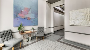 Eine moderne Lobby mit einem großen abstrakten Gemälde, einer Sitzecke mit zwei Stühlen, einem kleinen Tisch mit einer Pflanze und einem gemusterten Teppich.
