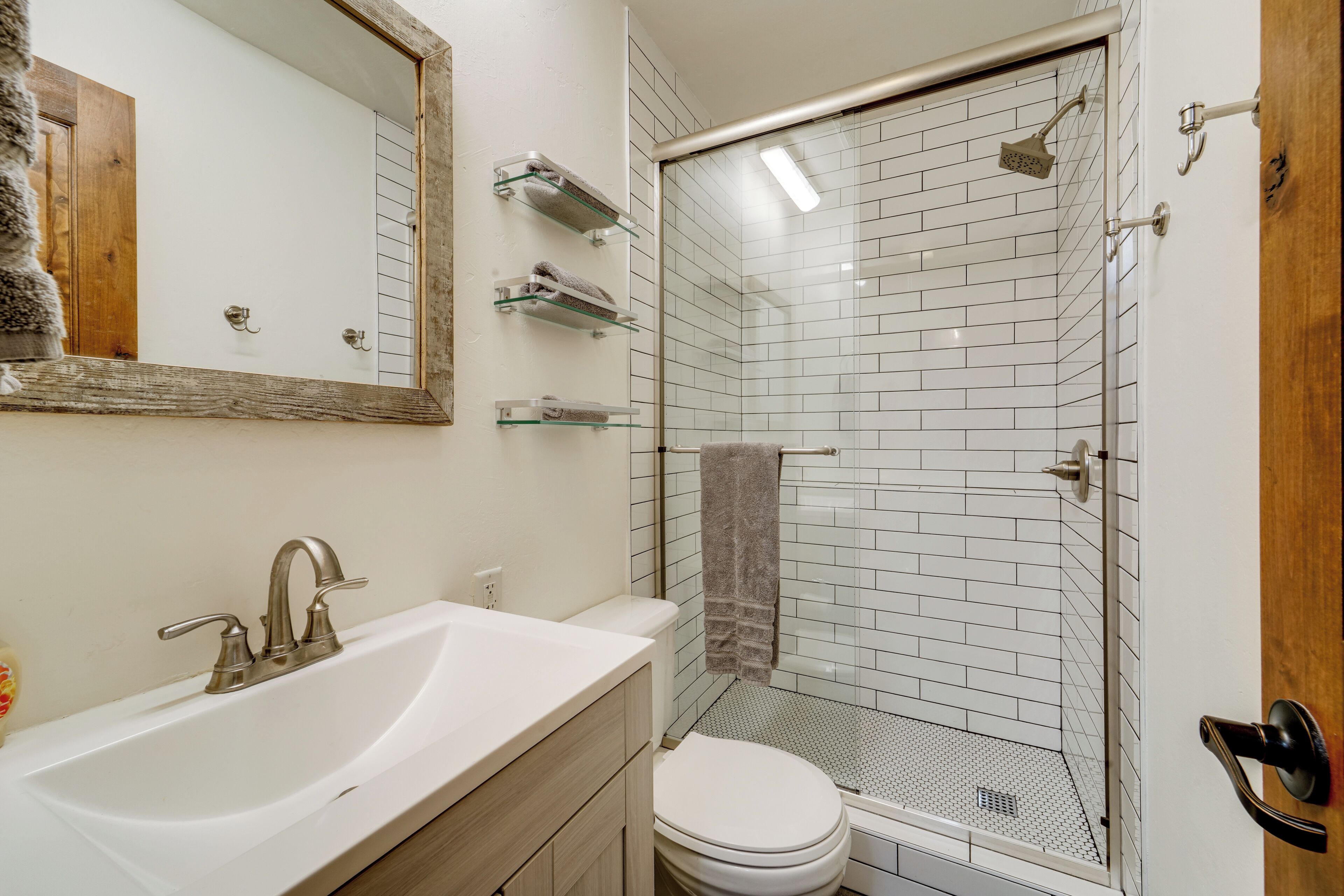 Een badkamer met een wit wastafelmeubel, toilet, douchecabine met glazen wanden en een spiegel.