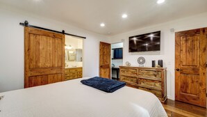 A bedroom with a large bed, wooden wardrobe, a dresser, a mirror, and a TV on the wall.