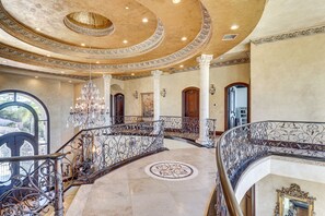 A grand interior with a curved staircase, ornate columns, and a chandelier. - Grand 9,000-sq-ft Estate! Luxurious Socal Getaway (La Mesa)