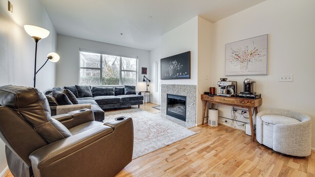 A modern living room with a leather sofa, a fireplace, a coffee table, and a dining area with a wooden table and chairs. - Condo 6 Mi to Lumen Field & Dtwn Seattle! (Seattle)