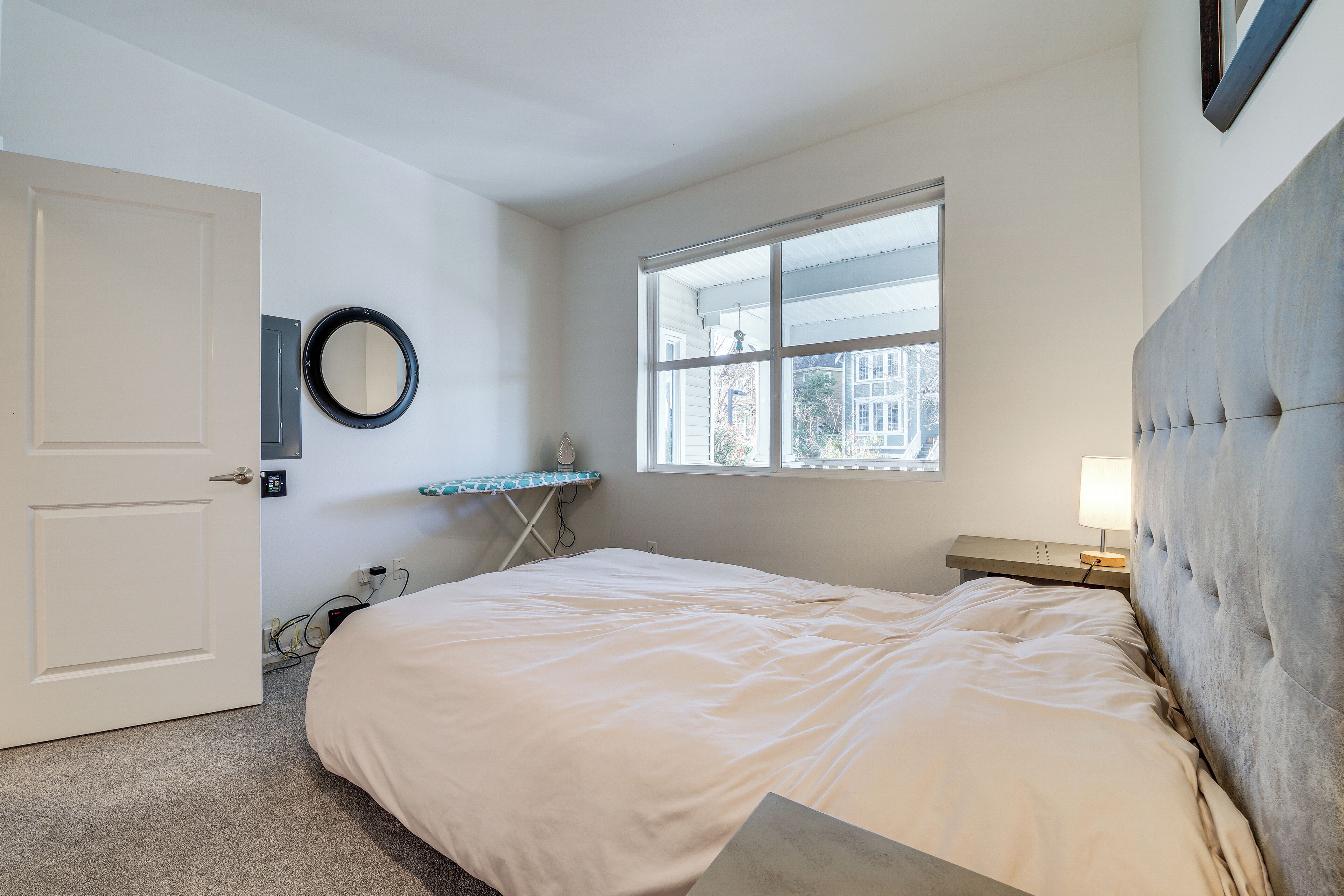 A bedroom with a bed, a window, a bedside table, and a mirror.