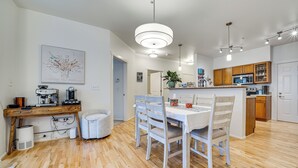 A modern kitchen with wooden cabinets, a dining area with a white table and chairs, and a hanging light fixture. - Condo 6 Mi to Lumen Field & Dtwn Seattle! (Seattle)