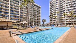A hotel pool area with a clear blue pool, lounge chairs, and palm trees. - Steps to Sand: Resort Escape on South Padre Island (South Padre Island)