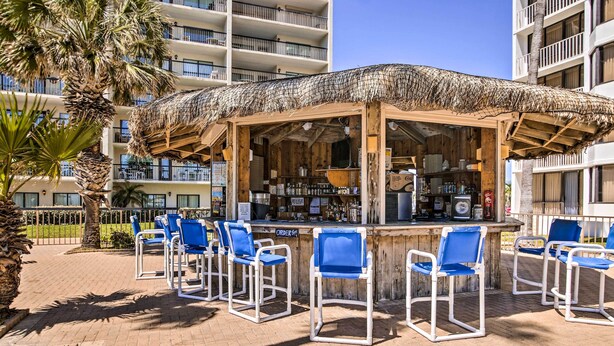 An outdoor bar area with a thatched roof, wooden bar counter, and blue chairs. - Steps to Sand: Resort Escape on South Padre Island (South Padre Island)