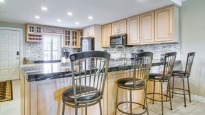 A kitchen with wooden cabinets, a granite countertop, and four bar stools. - Steps to Sand: Resort Escape on South Padre Island (South Padre Island)